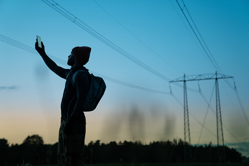 En person står i solnedgången och håller upp sin telefon mot himlen.
