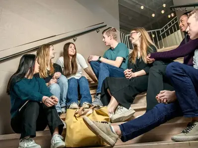 En grupp elever sitter på en trappa inomhus och har ett avslappnat samtal tillsammans.