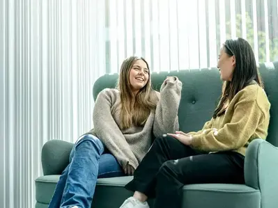 Två elever sitter i en soffa och pratar och skrattar tillsammans.